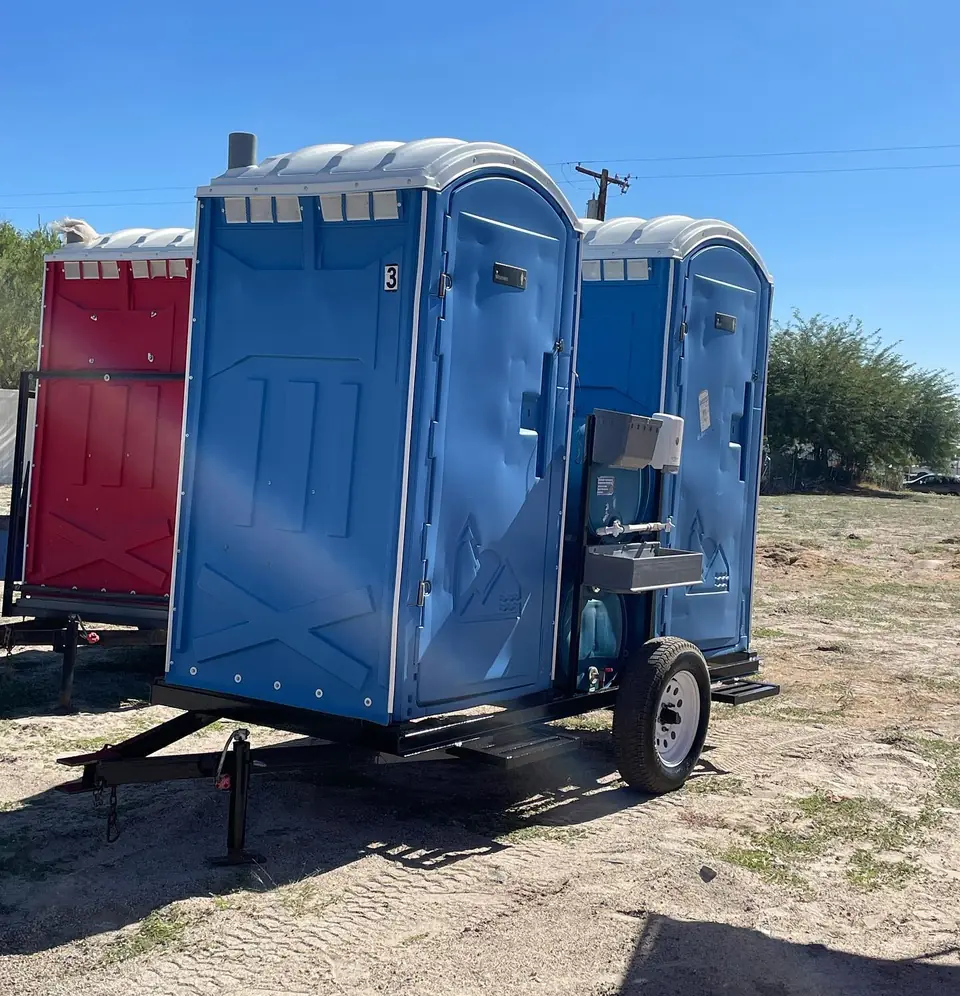 Blue and red portable toilets mounted on a towable single-axle trailer