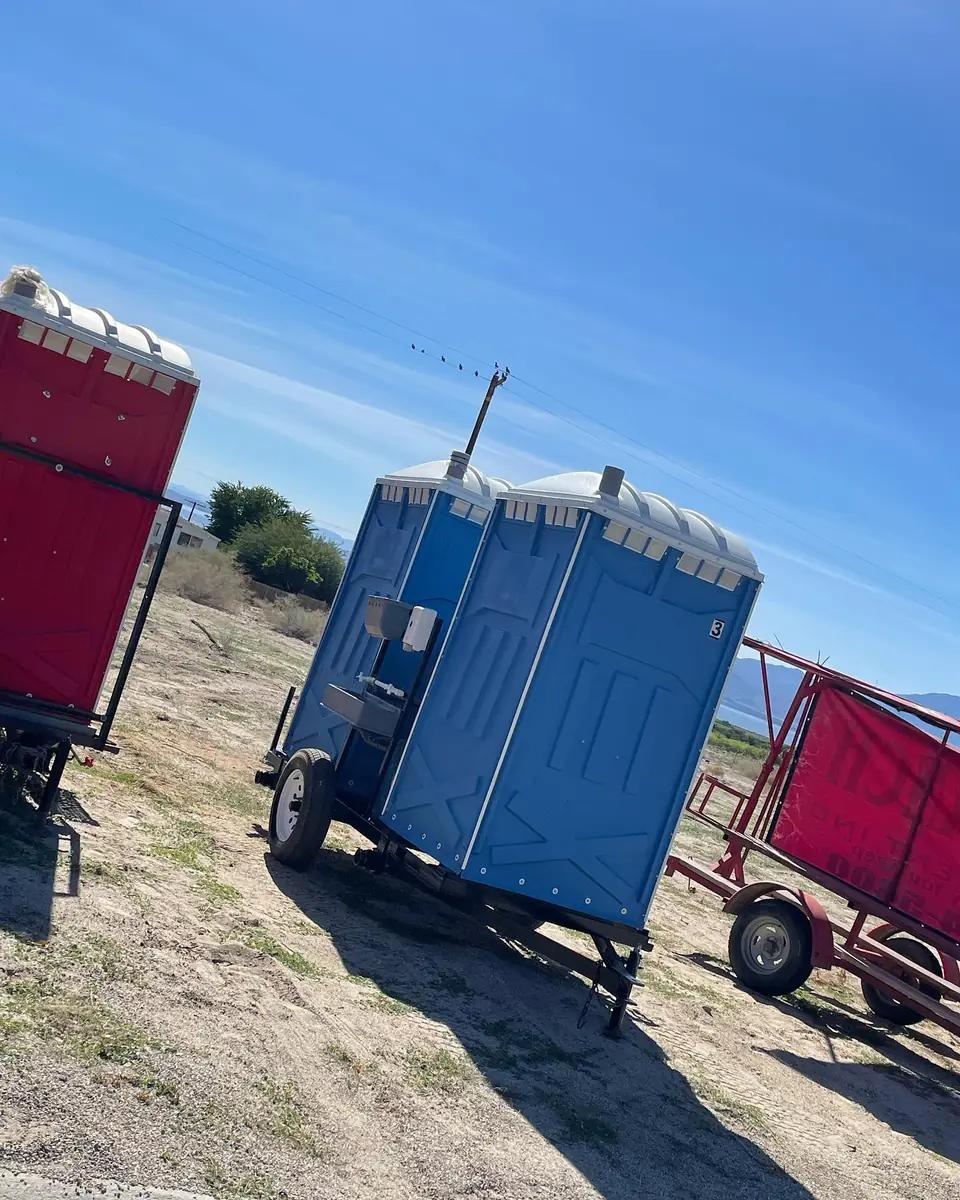 Two towable porta potty trailers parked in an open dirt field